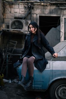 Young woman sitting on a vintage car in an urban Tehran setting.