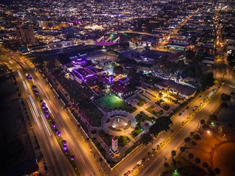 Vibrant aerial night view of Ensenada cityscape with illuminated streets and buildings.