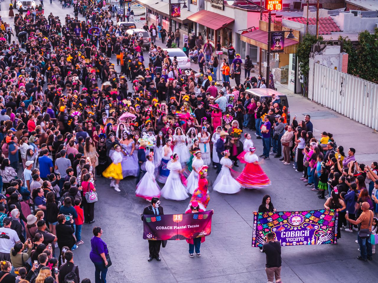 a colorful day of the dead parade with costumes and crowds in a lively