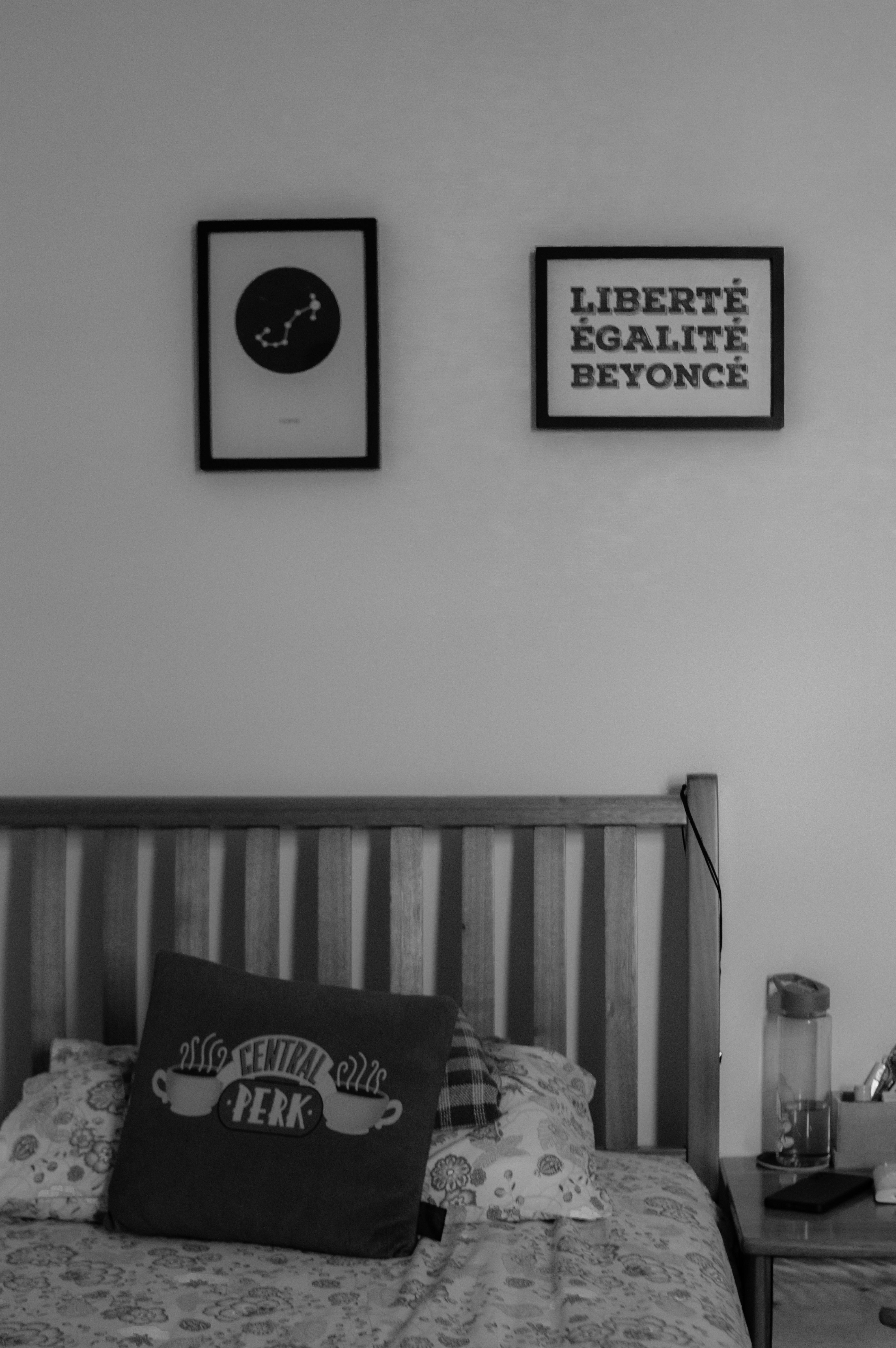 Black and white image of a cozy bedroom featuring wall art and a Central Perk cushion.