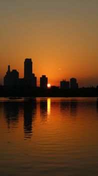 A serene sunset over a city skyline with reflections on water, creating a dramatic silhouette.