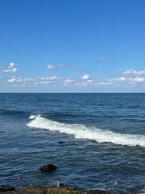 Free Calm ocean waves gently lap against the shore under a clear blue sky. Stock Photo