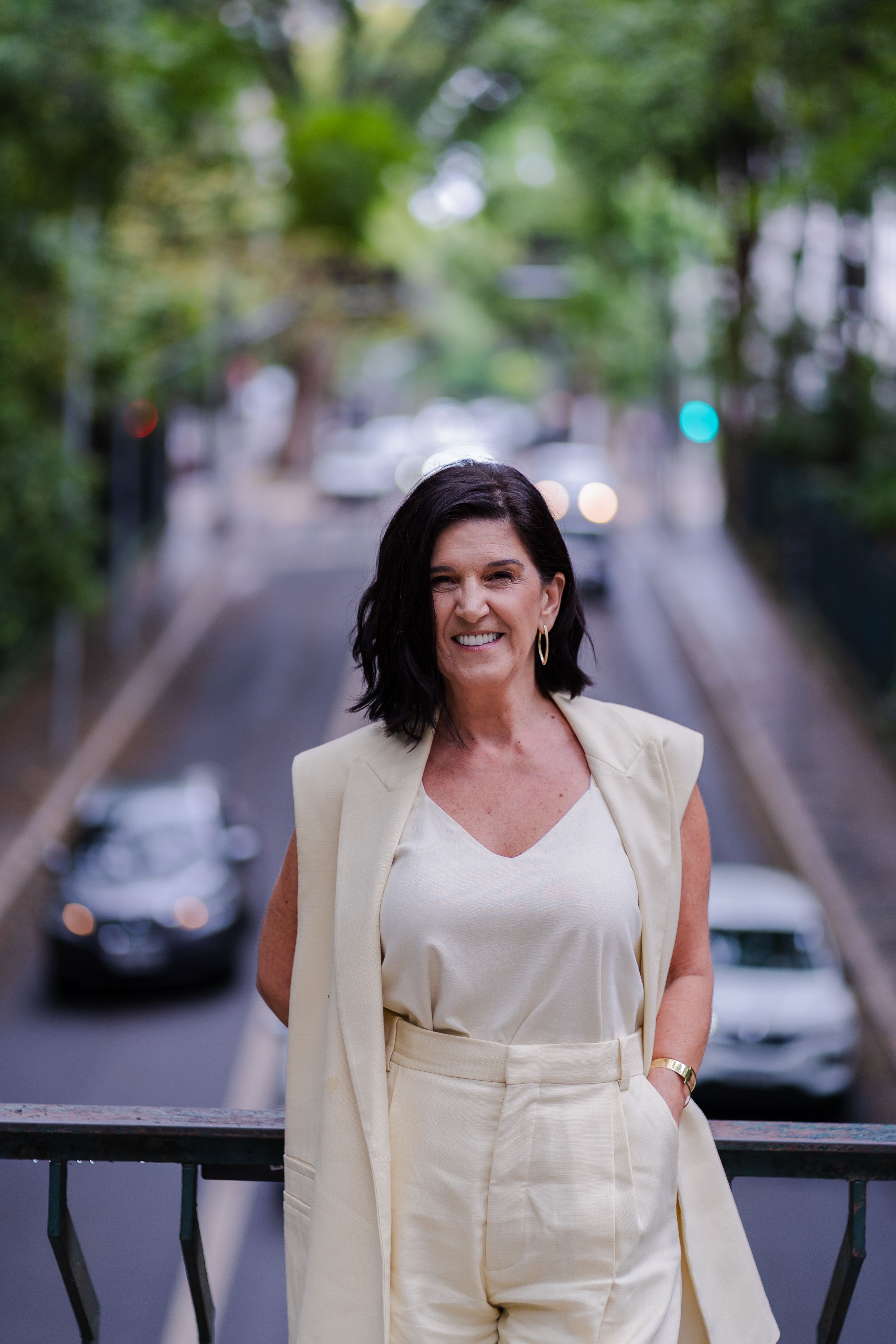 Smiling woman in neutral attire stands on a city bridge with blurred traffic backdrop.