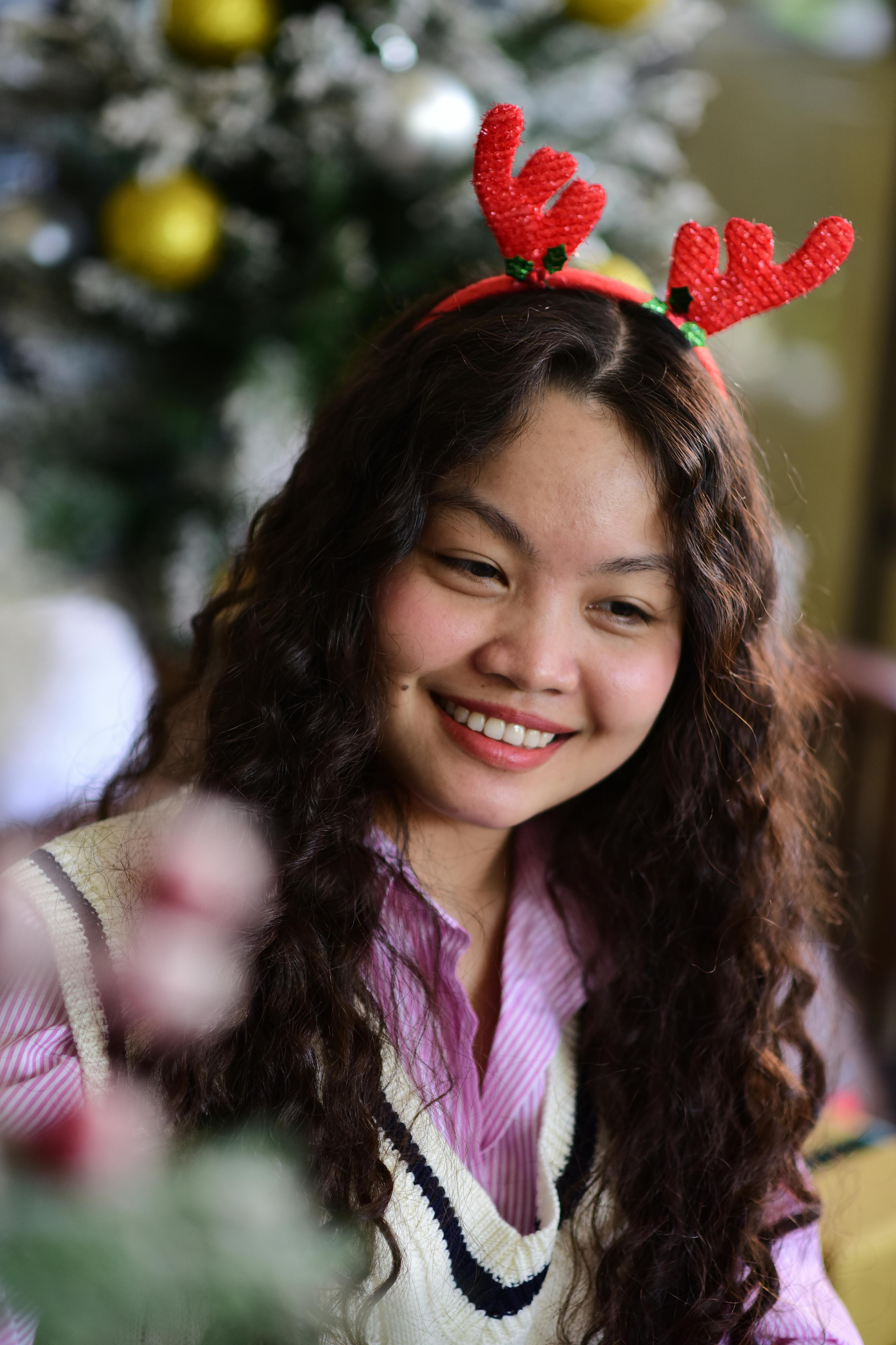De franc Una dona jove amb banyes de ren celebra les festes nadalenques a l'interior, a prop d'un arbre de Nadal decorat. Foto d'estoc