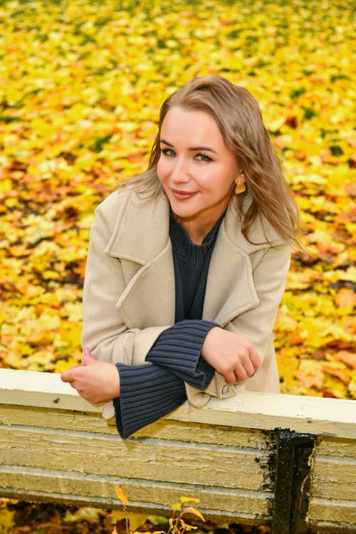 Free A woman in a beige coat smiles among vibrant autumn leaves. Stock Photo