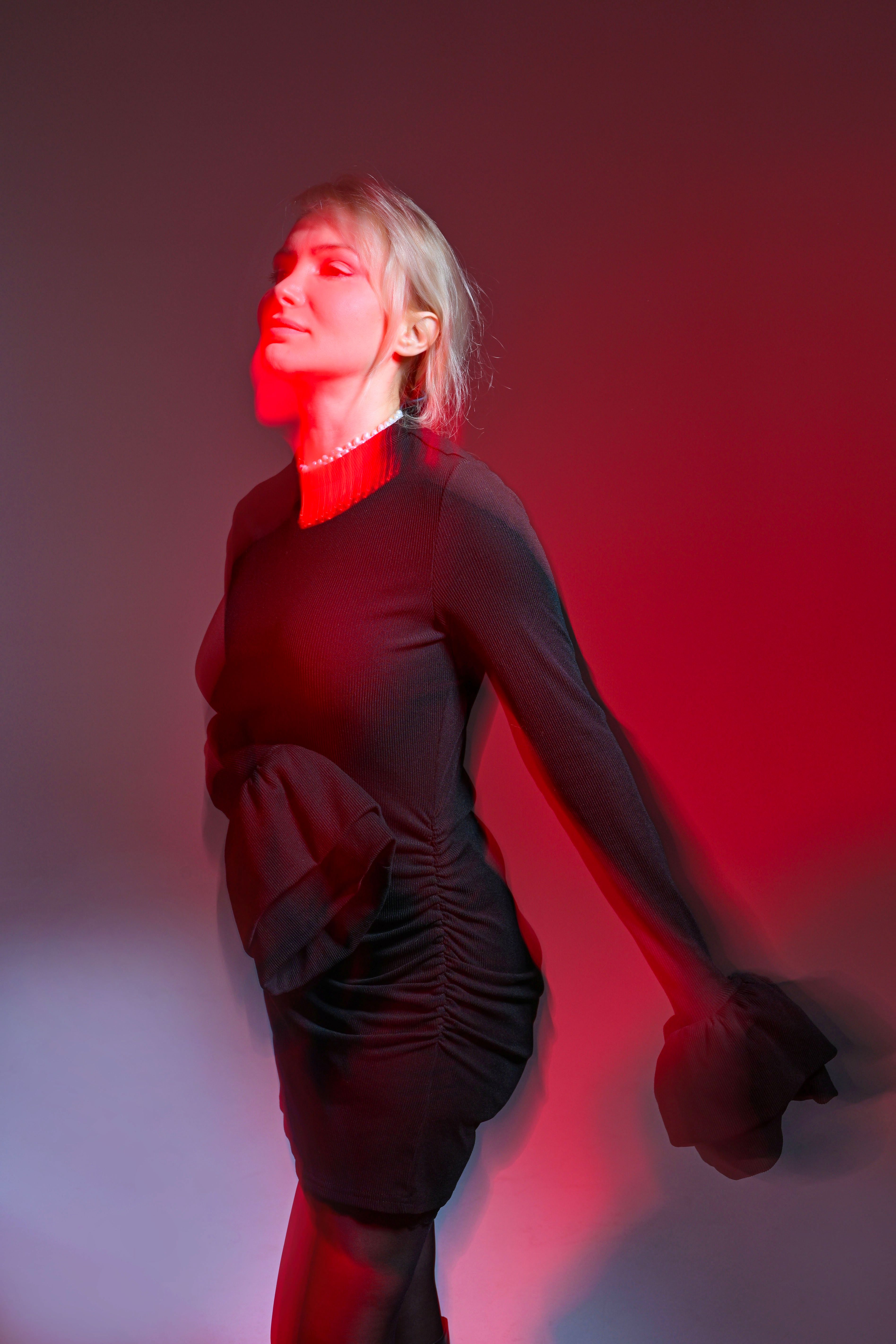 Woman in a black dress poses under moody red lighting, exuding elegance and mystery.