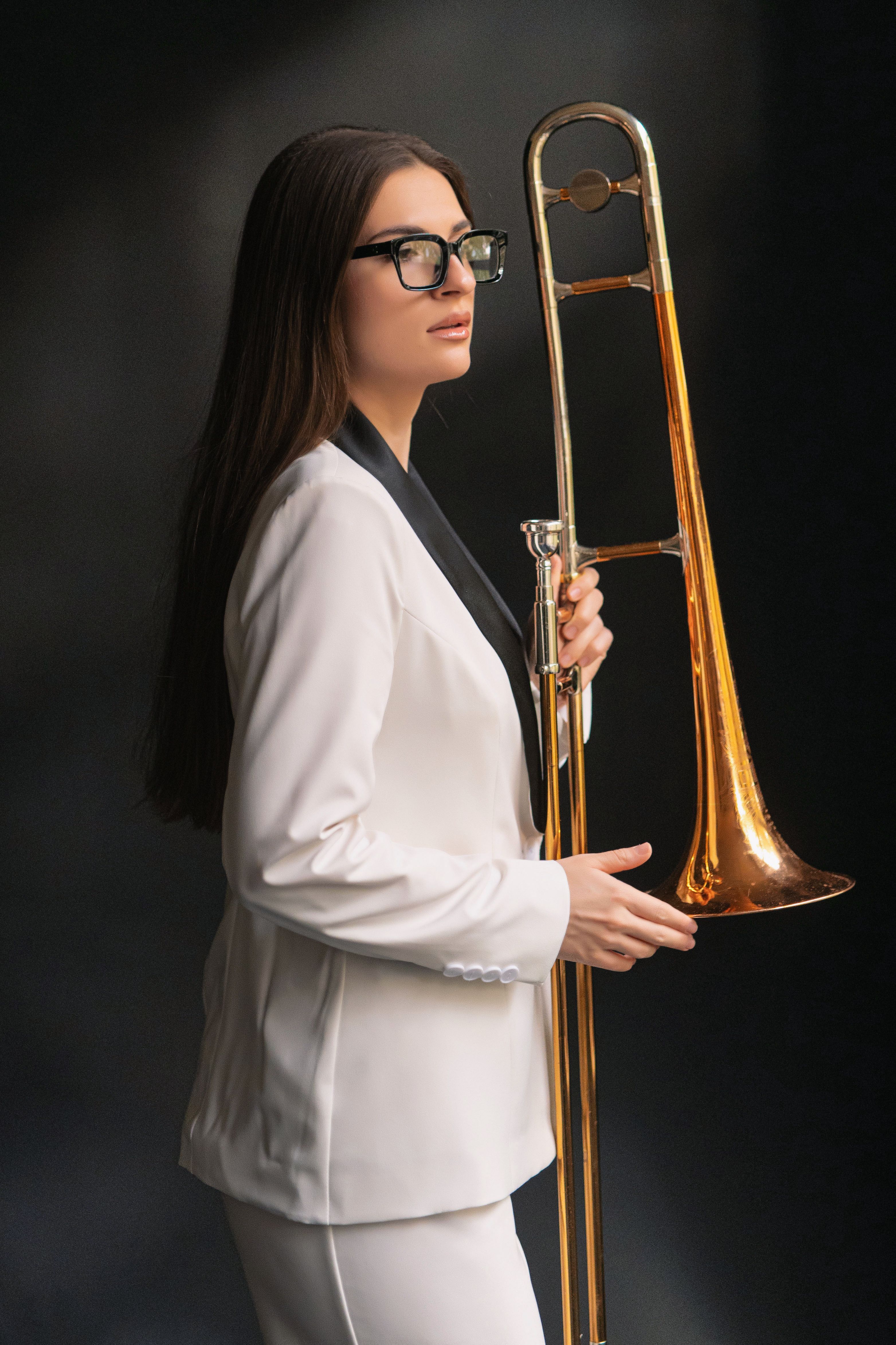 Stylish woman in a white suit holding a trombone, showcasing elegance and musical passion.