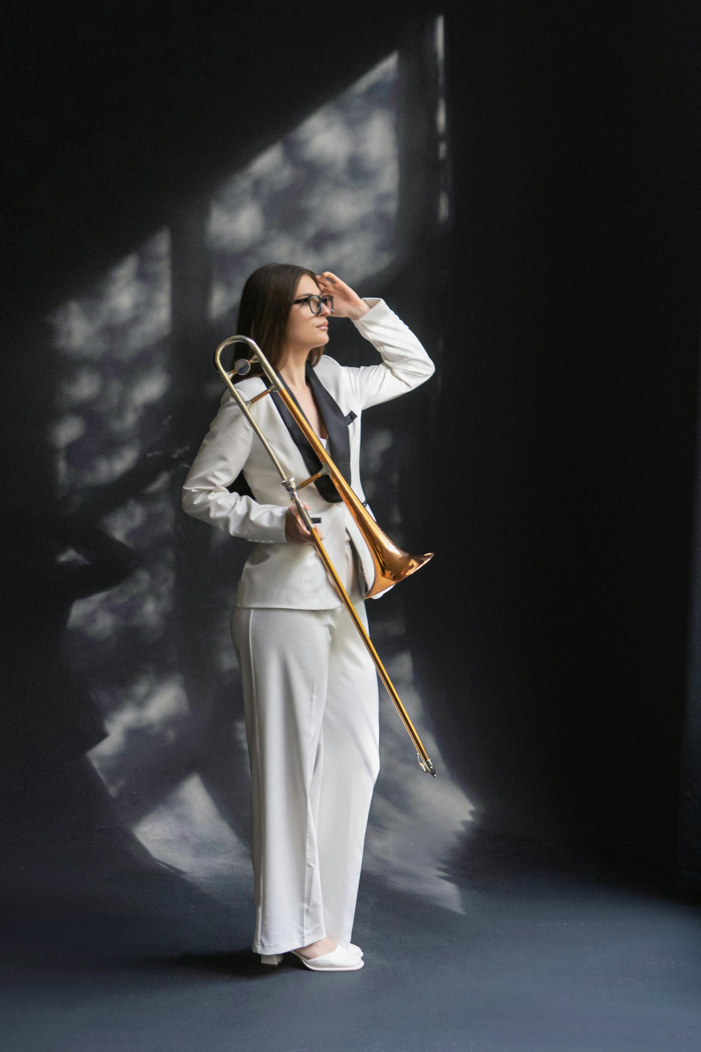 Portrait of a woman in a white suit with a trombone in a moody setting.