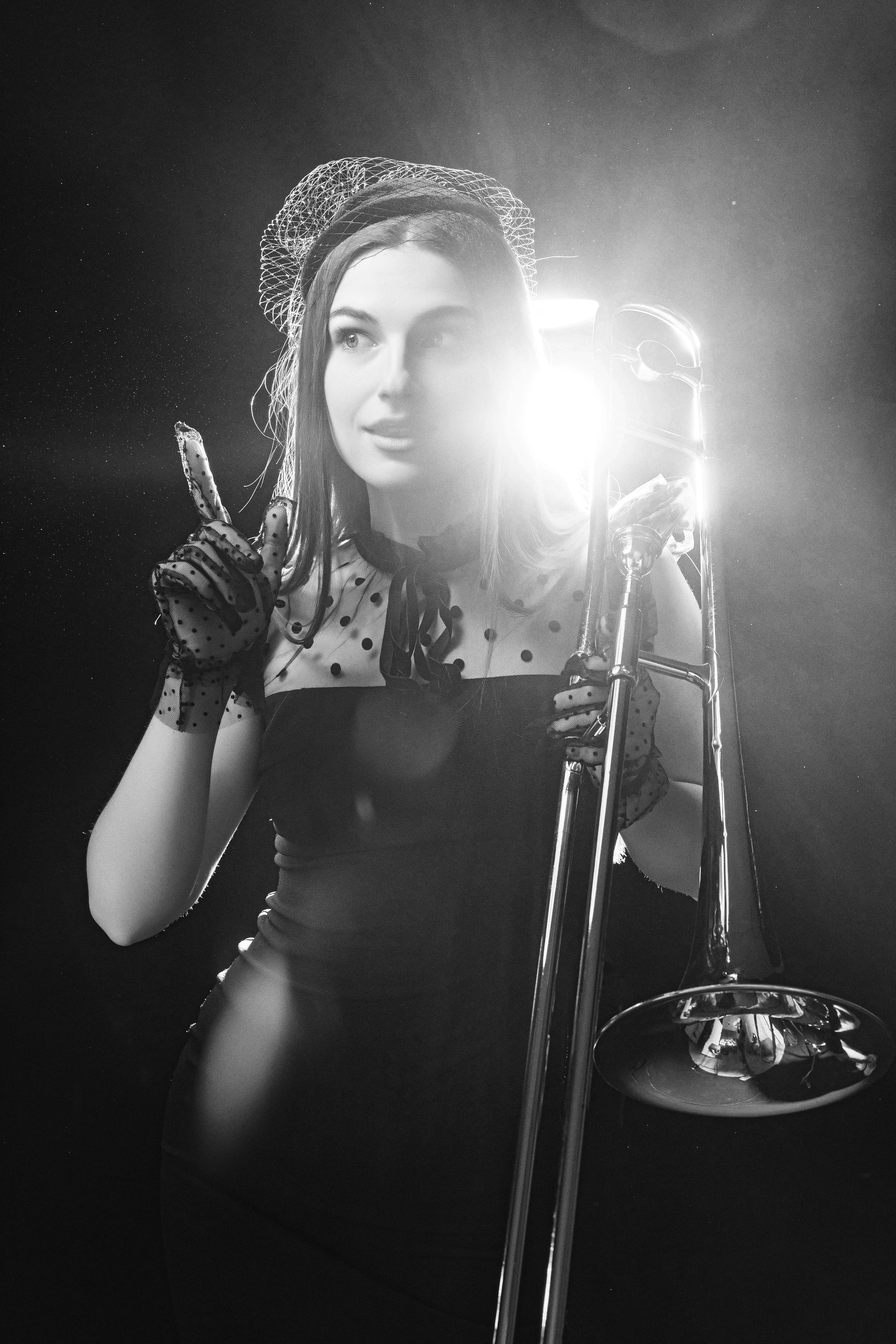 A stylish woman in vintage attire poses with a trombone, exuding elegance in black and white.