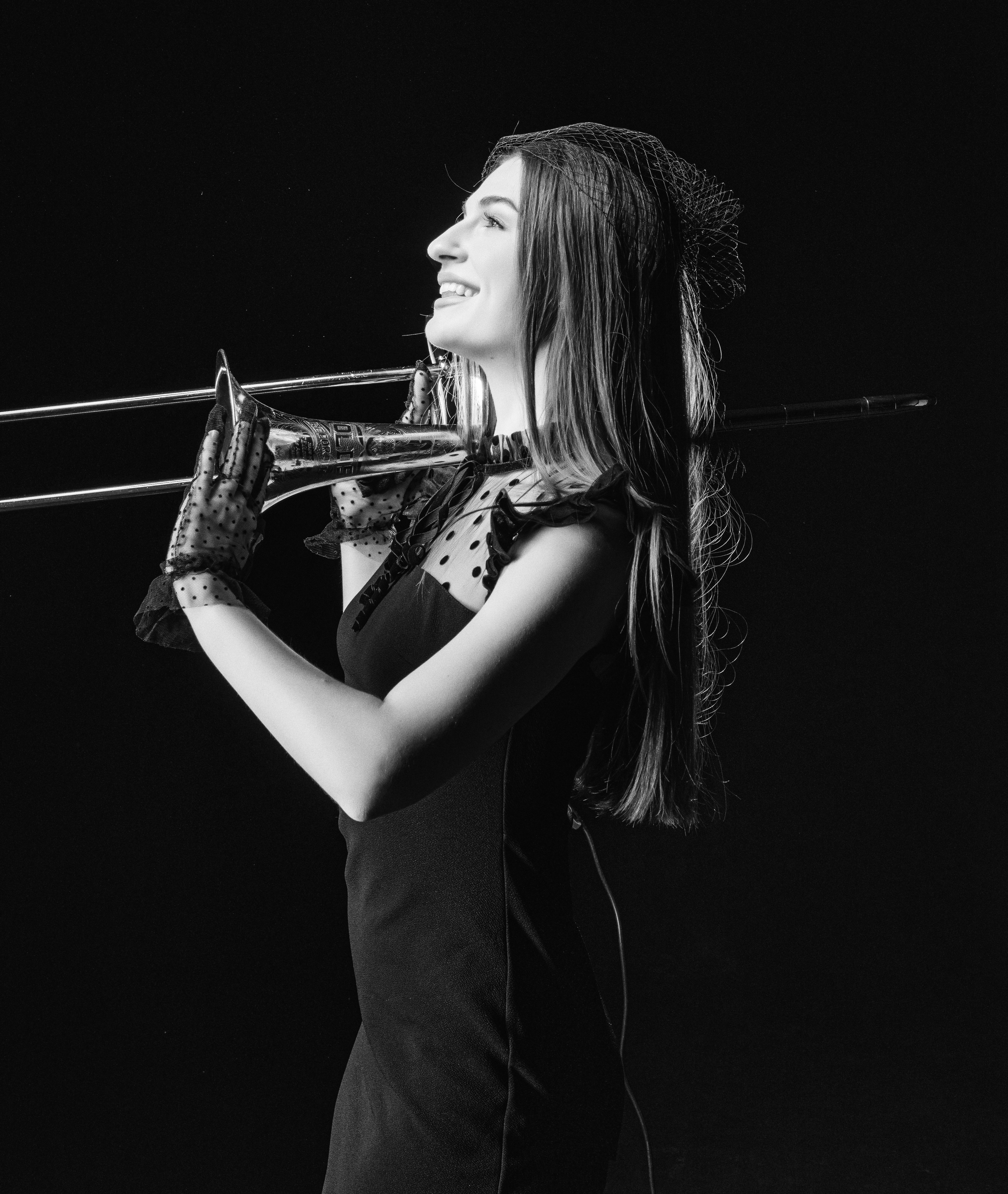 Portrait of an elegant woman in vintage attire playing a trombone, captured in classic black and white.
