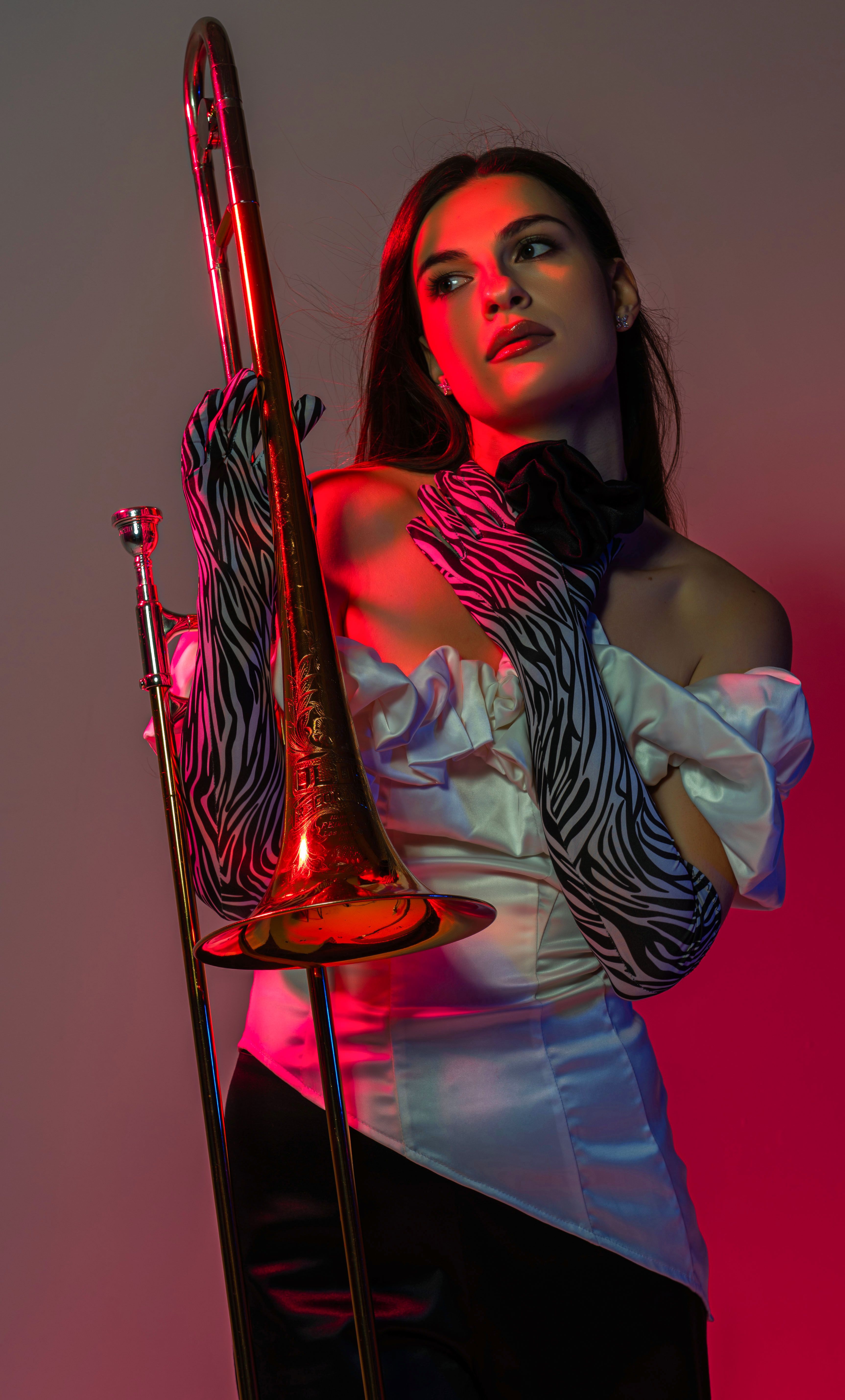 Elegant woman with zebra gloves and trombone in vivid studio lighting.