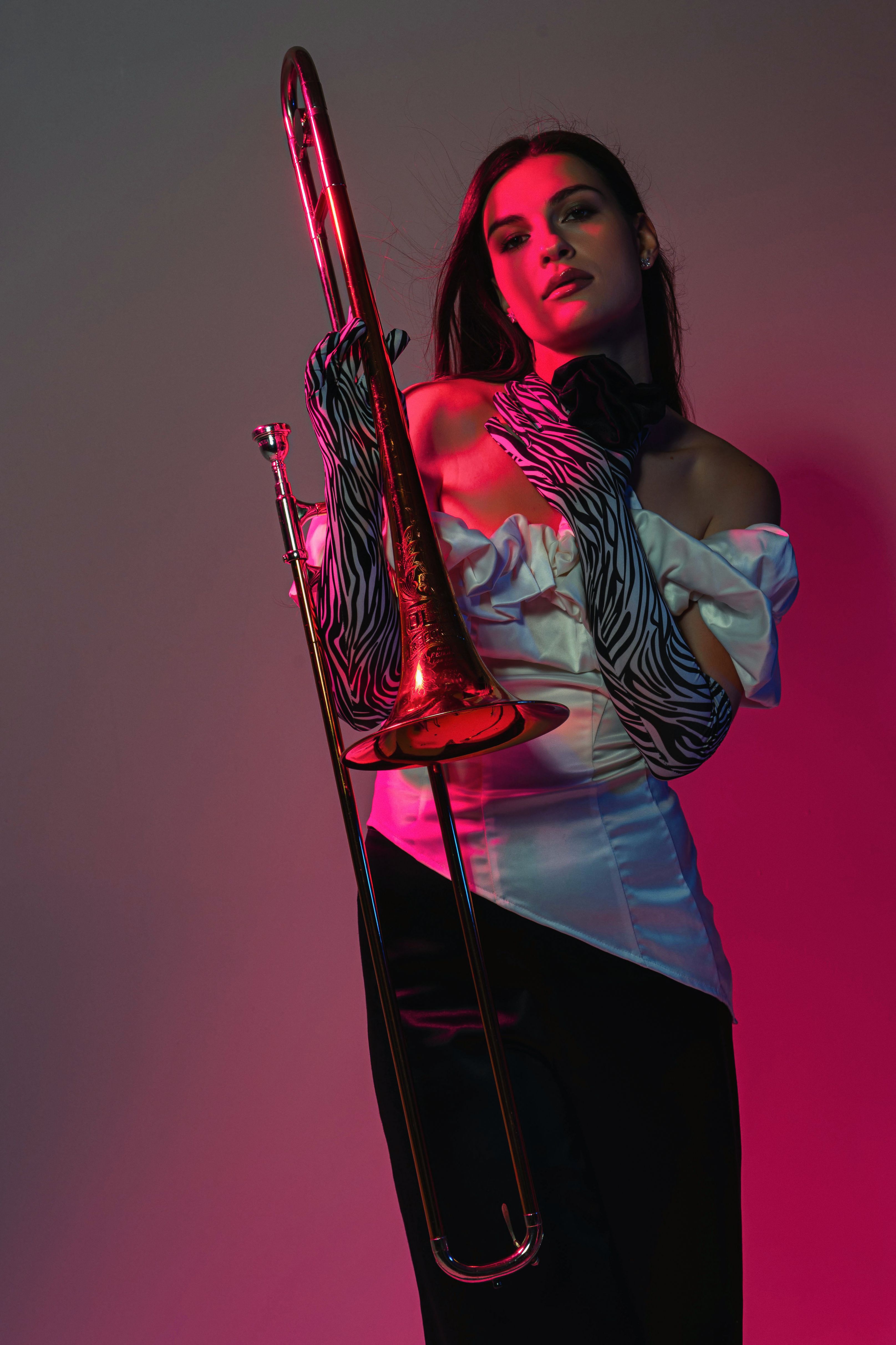 Stylish woman holding a trombone with dramatic lighting in a studio setting.