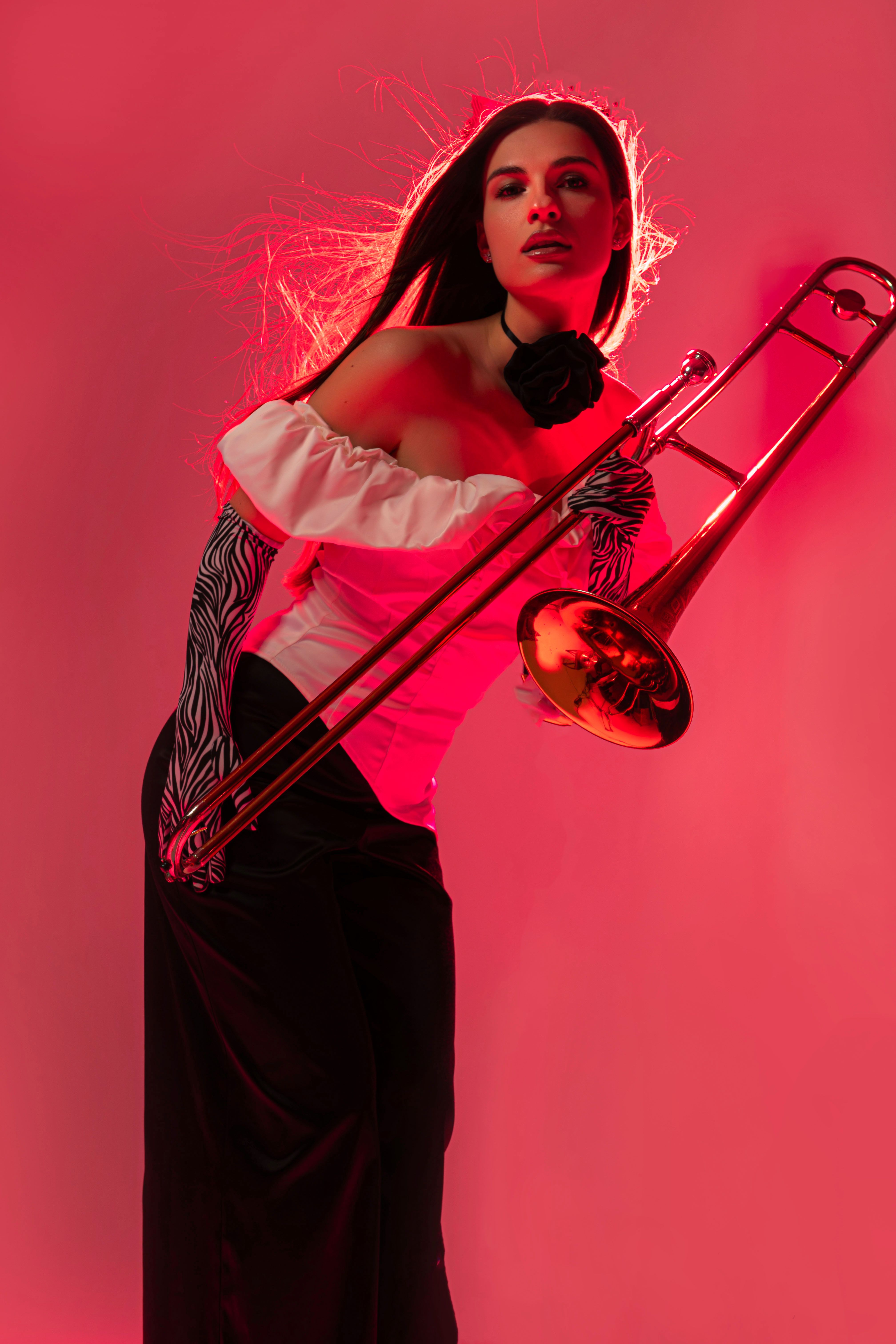 Stylish young woman holding a trombone in a vibrant red studio setting, showcasing elegance and musical passion.
