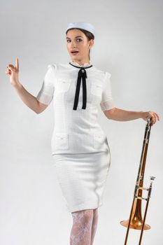 Stylish woman in a vintage white dress posing with a trombone, showcasing a retro vibe.