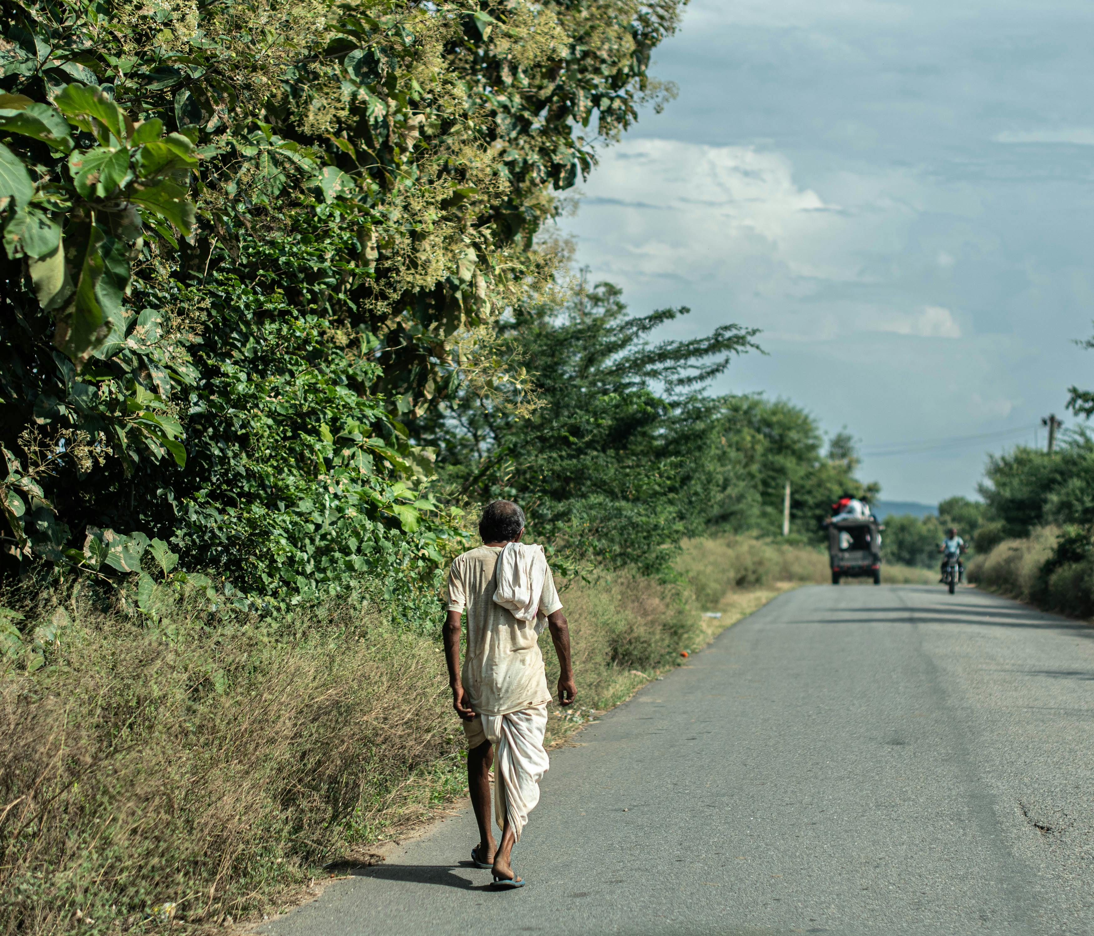 An elderly man in traditional attire walks along a rural road in Pushkar, Rajasthan, India.