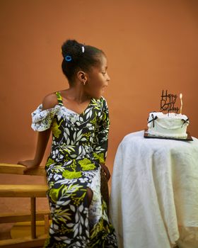 A young girl in a vibrant dress celebrates her birthday with a cake on a warm background.