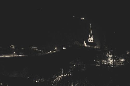 Free A serene nighttime view of a church with an illuminated spire and surrounding village lights. Stock Photo