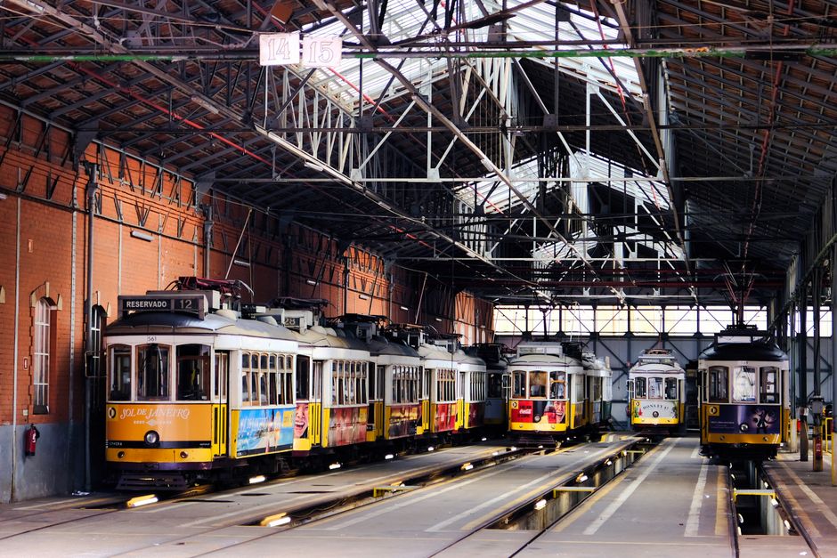 A row of historic yellow trams parked inside a Lisbon depot showcasing vintage urban transport. — Elétrico, Portugal.