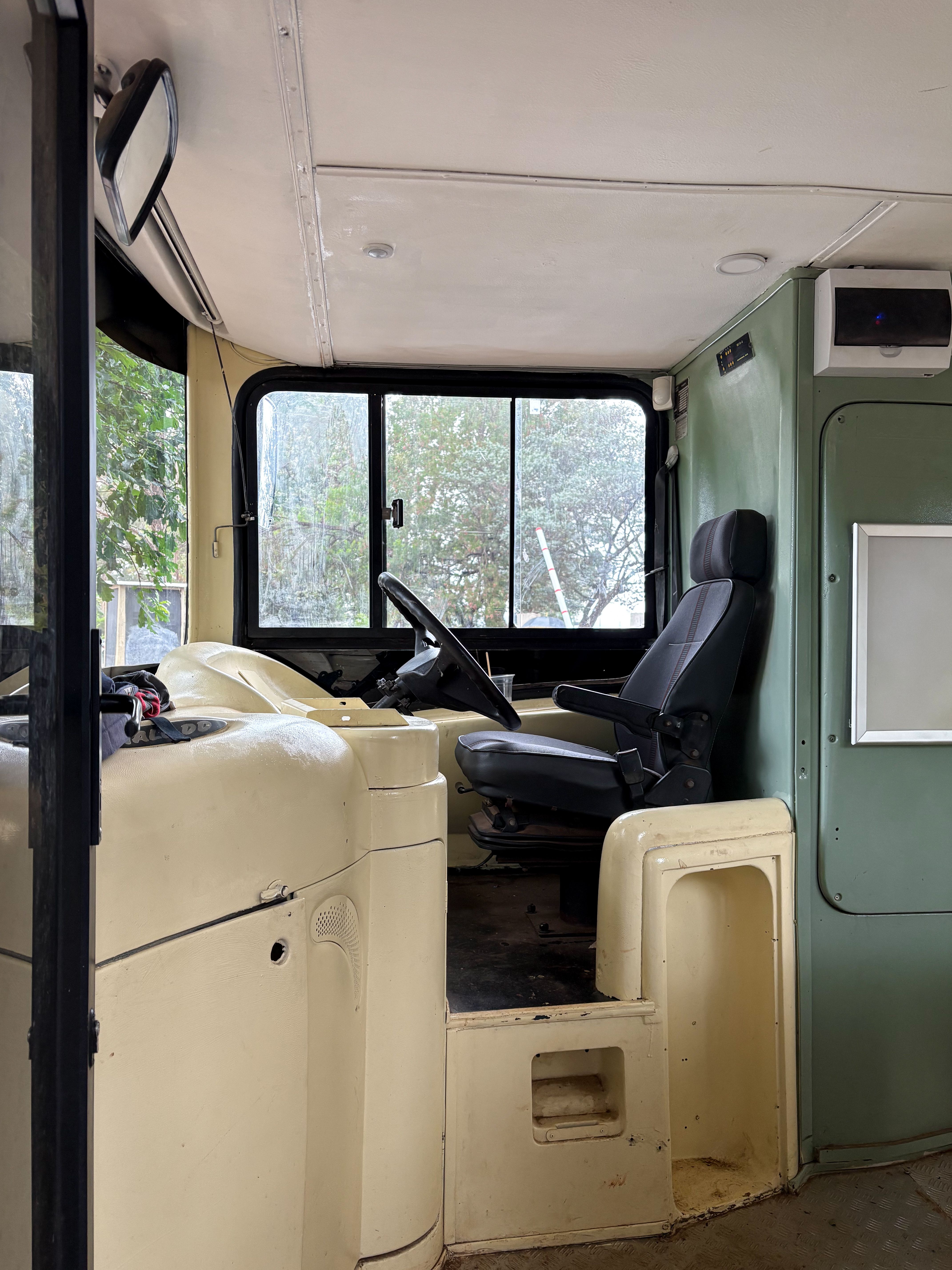 Interior view of an empty bus showcasing the driver's seat and dashboard. Bright natural light streams through the windows.