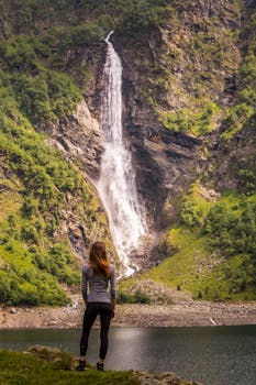 A woman stands by Gavarnie Falls, a majestic waterfall in Oô, Occitanie, France.