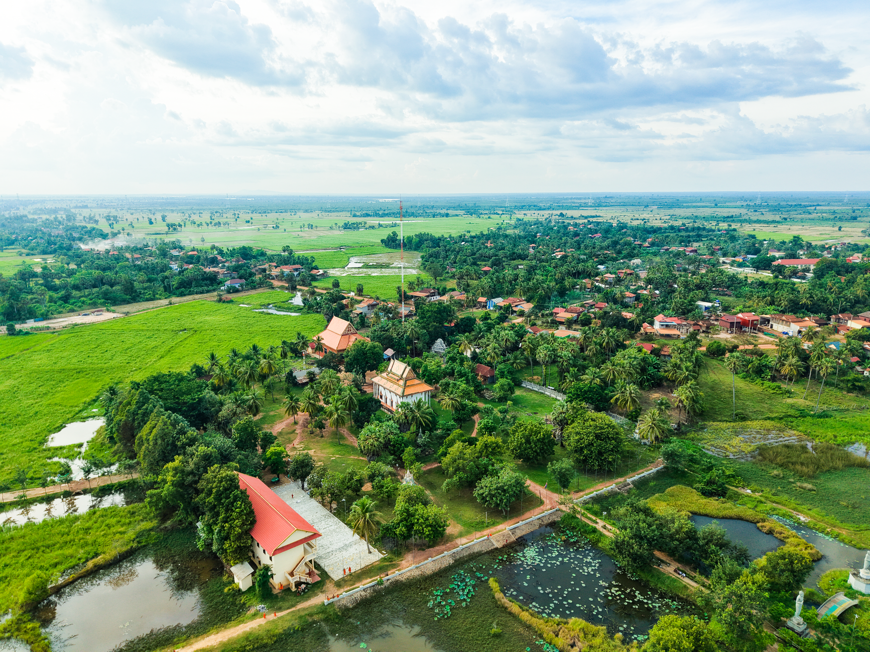 Scenic aerial view of lush Cambodian countryside with traditional temples and vast green fields.