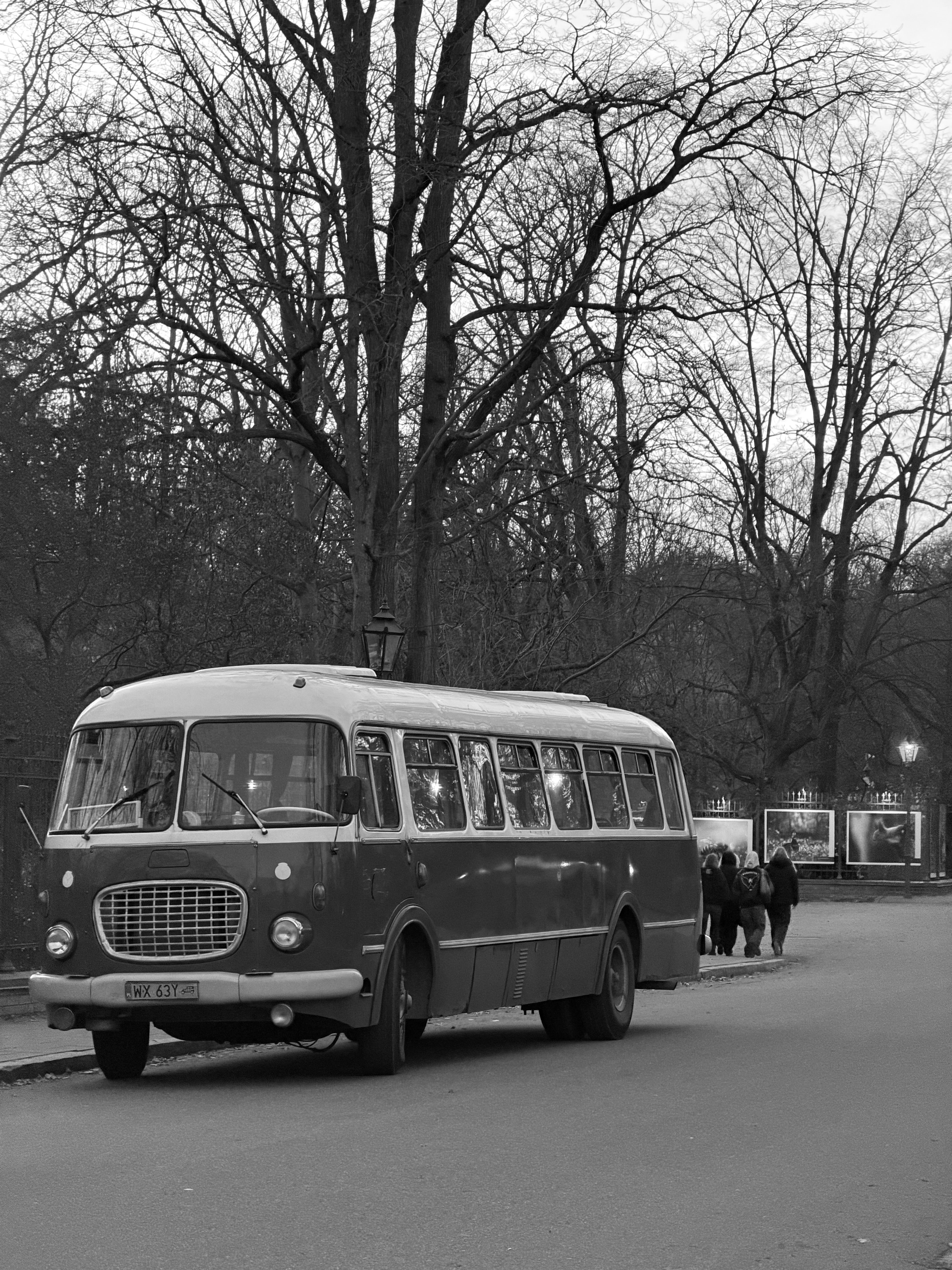 Black and white photo of a vintage bus in Warsaw, Poland, with bare winter trees.