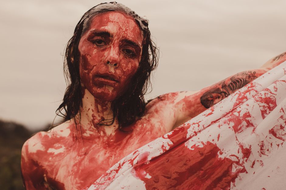 A striking artistic portrait featuring a person covered in red paint outdoors.