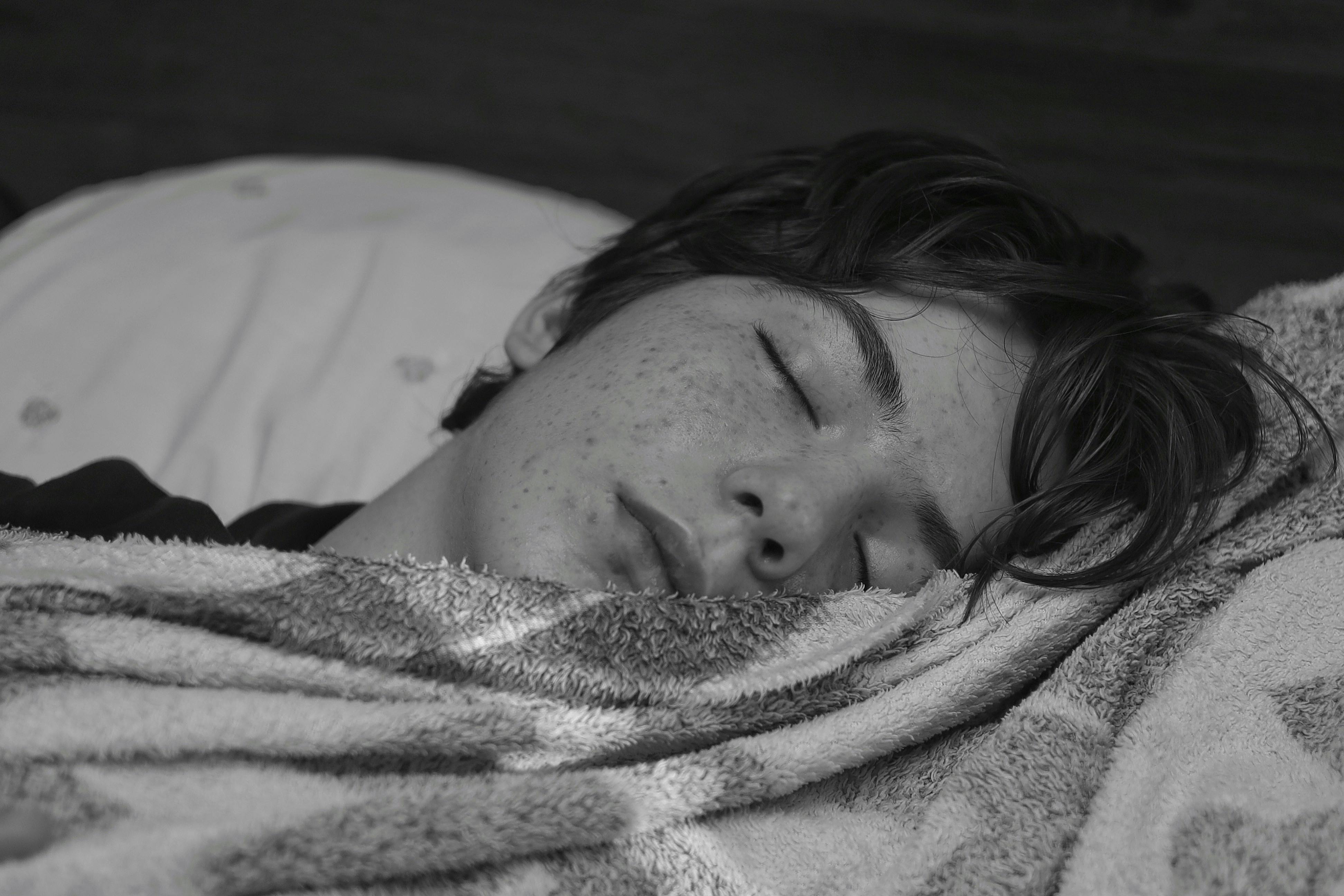 Black and white photo of a teenage boy sleeping peacefully wrapped in a blanket.