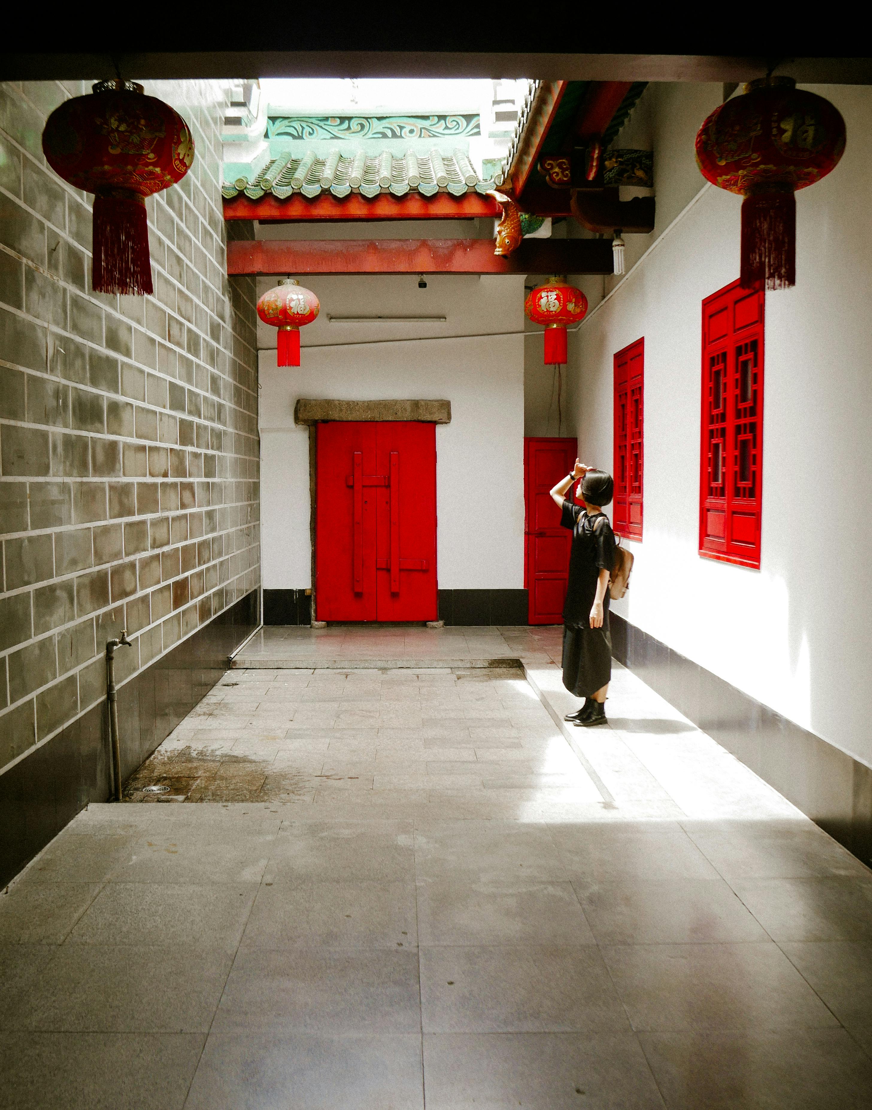 A person stands in a sunlit courtyard with red lanterns and traditional architecture.