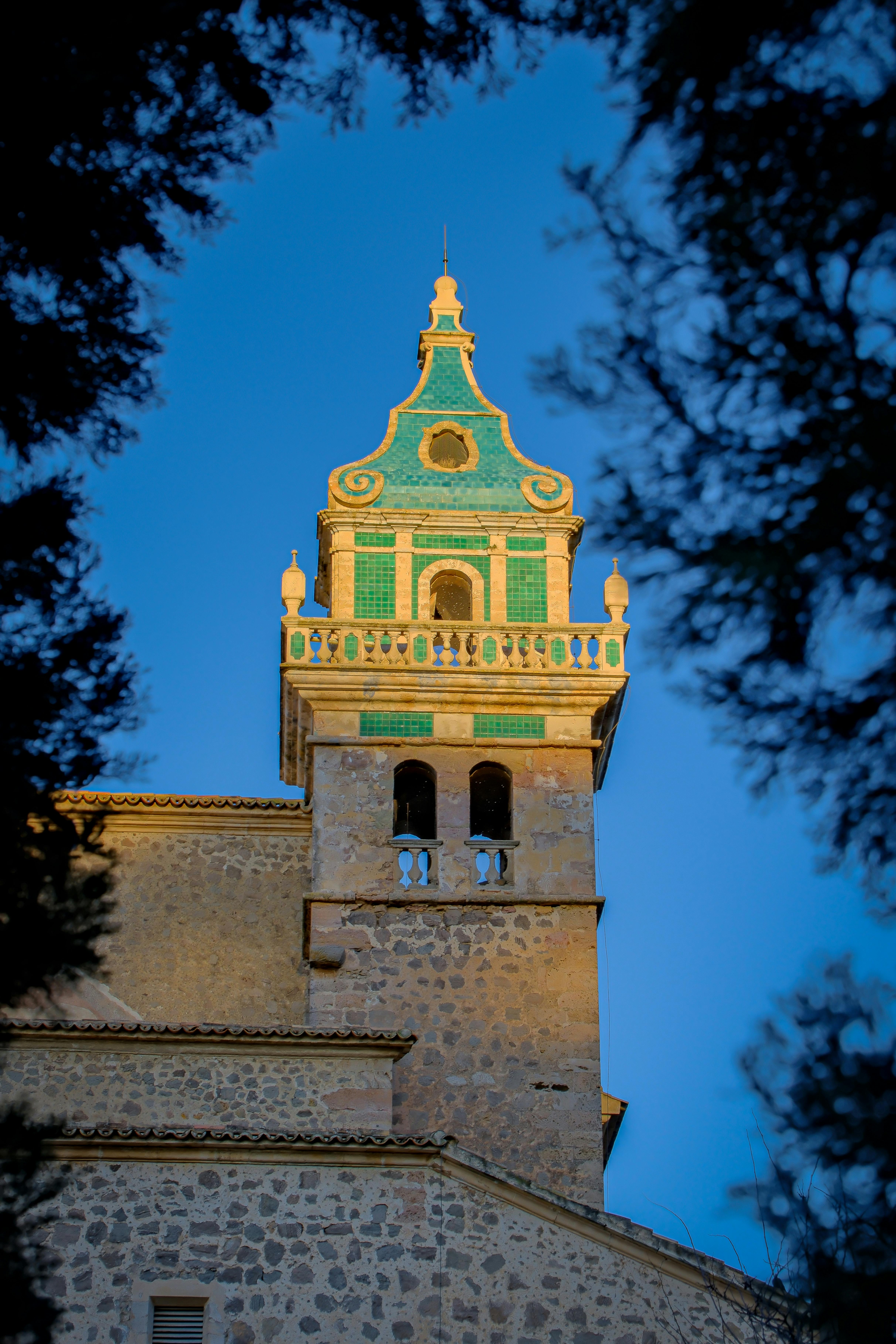 Beautiful view of Valldemossa Charterhouse tower captured at sunset, framed by trees.