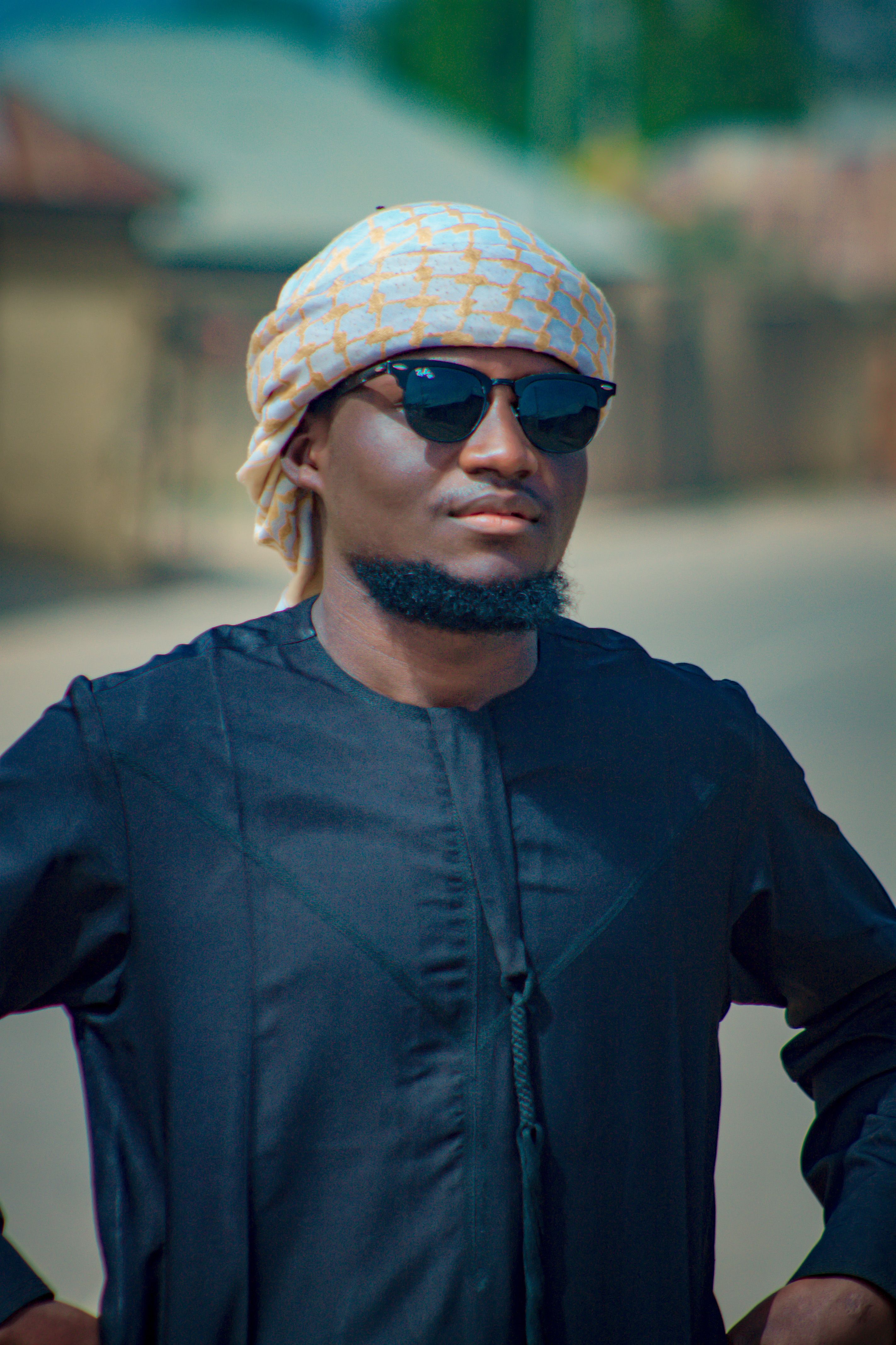 Stylish man wearing sunglasses and traditional attire outdoors in sunny weather.
