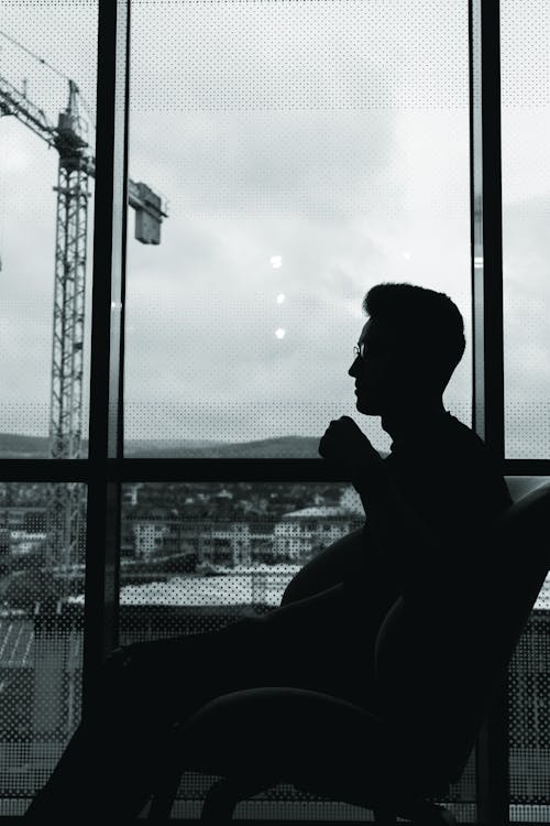 Silhouette of Man Sitting Beside Window