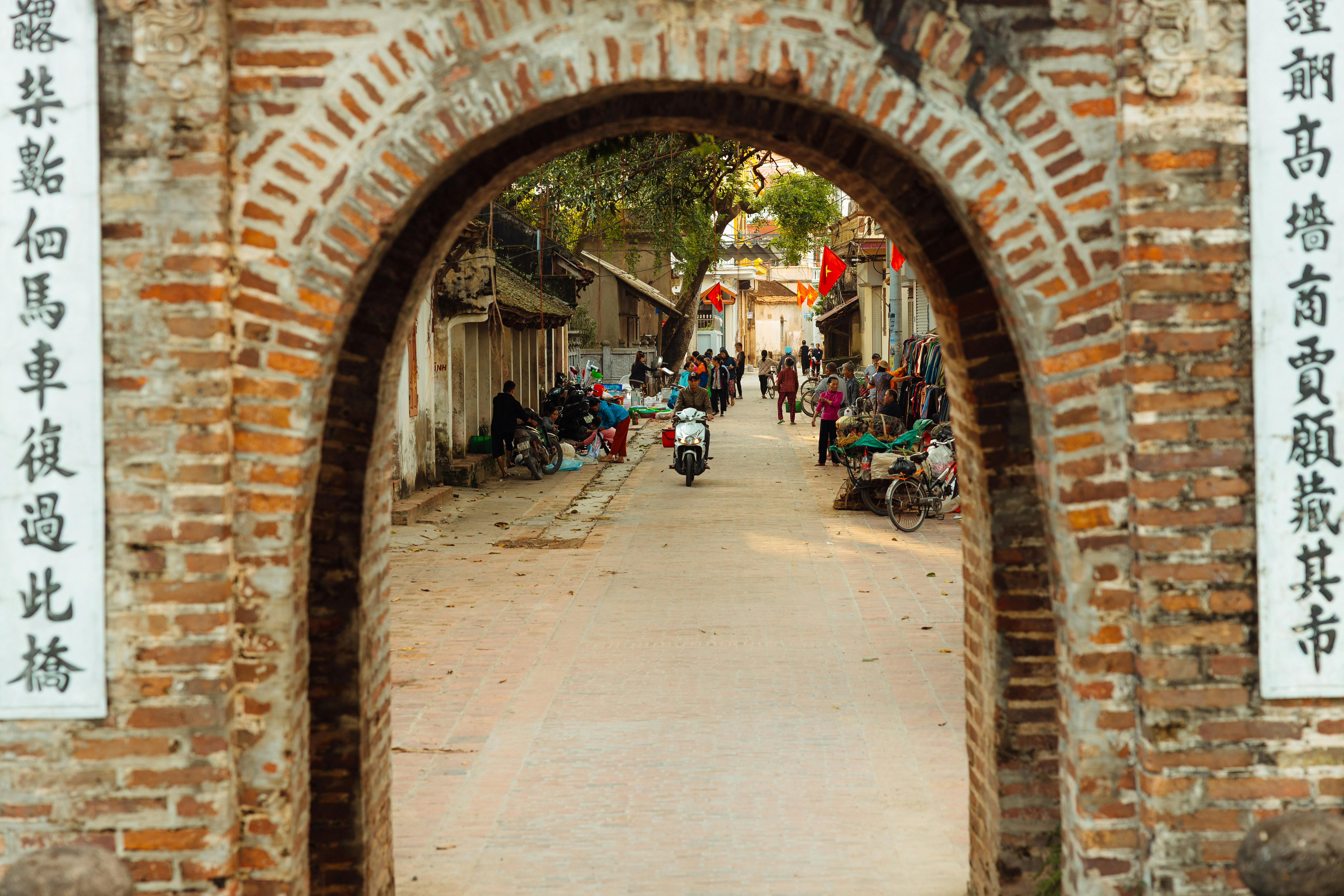 A vivid street scene through a historic brick archway, showcasing local marketplace activity and architecture.
