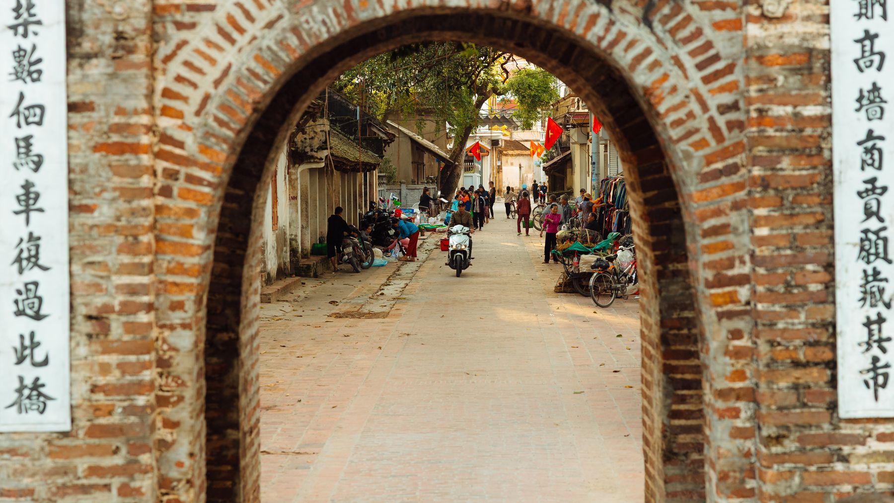 Khung cảnh đường phố sống động qua một vòm gạch lịch sử, thể hiện hoạt động chợ búa và kiến trúc địa phương.
