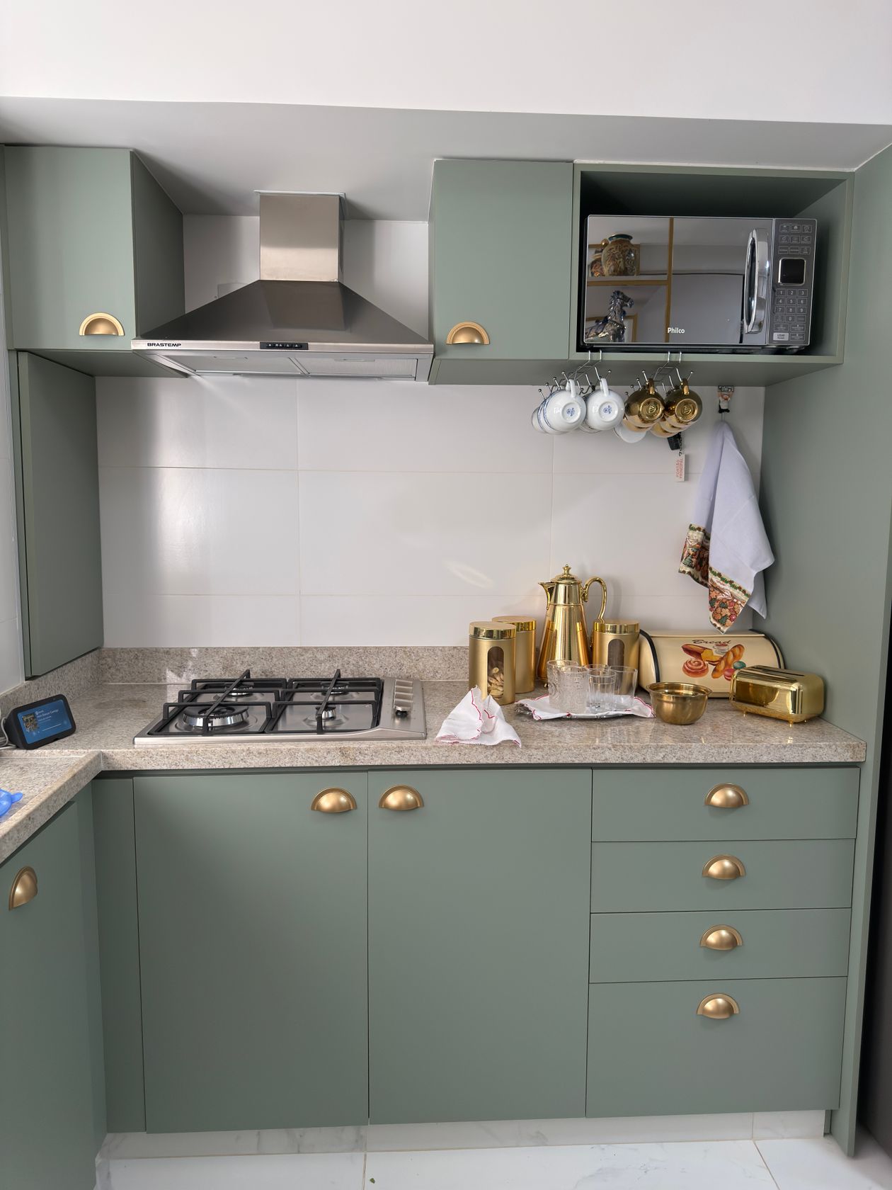 Sage green kitchen with brass cup pulls on the drawers