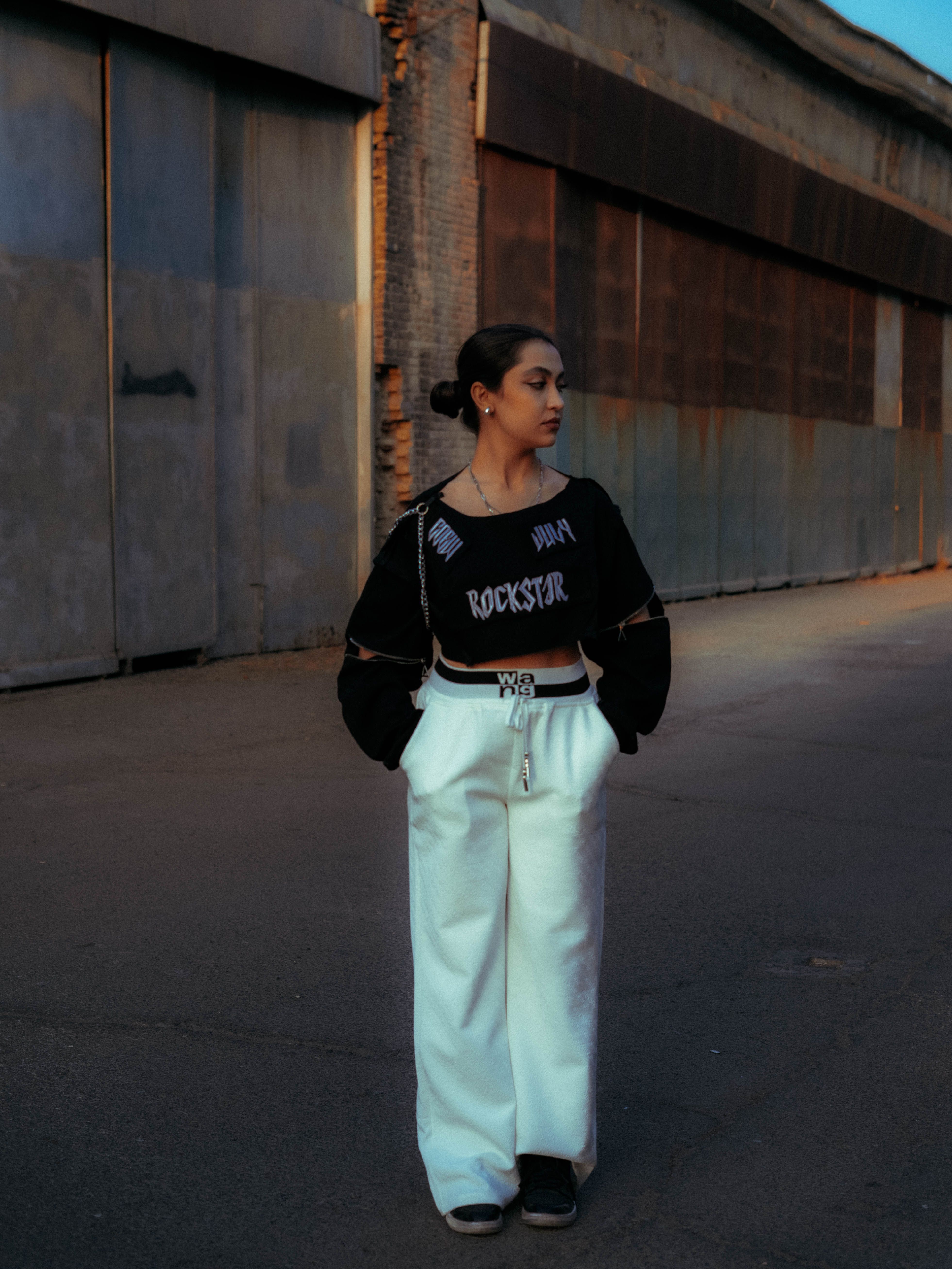 Young woman in streetwear fashion poses in an urban alley during twilight