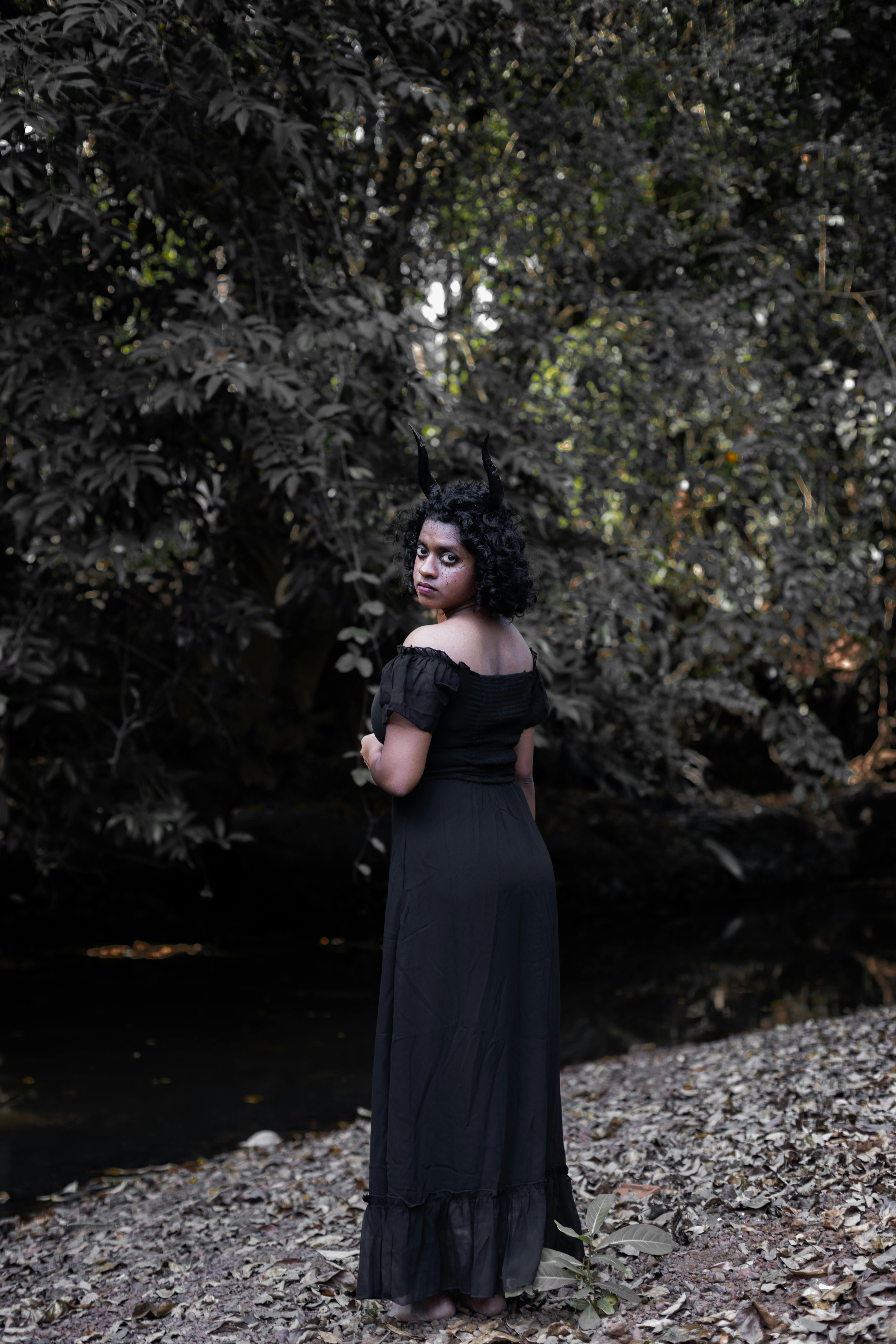 Gratuit Une femme en robe gothique se tient dans une forêt sombre, près d'un ruisseau, dégageant un mystère. Photos