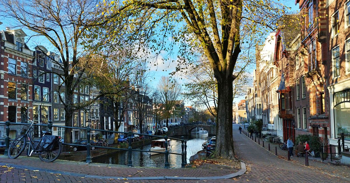Picturesque autumn view of Amsterdam canal with bicycles, trees, and historic architecture.