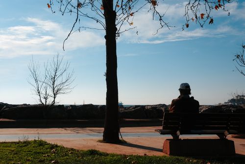 Free An individual sitting alone on a bench by the sea, embracing solitude in autumn. Stock Photo