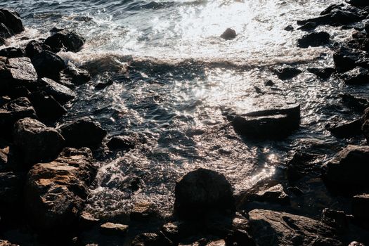 Waves gently crash on a rocky shoreline under the warm sunlight.