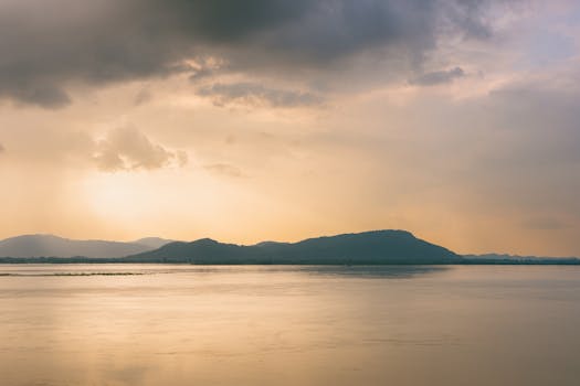 Peaceful sunset scene over the Brahmaputra River in Assam, India, with calm waters and hilly backdrop.
