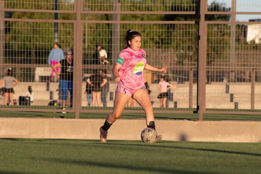 Young female soccer player dribbling the ball during a match on a sunny day.