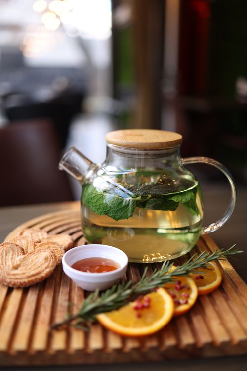 Free Glass teapot with herbal tea, orange slices, and rosemary on wooden board. Stock Photo