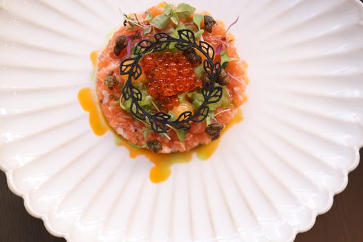 Delicious salmon tartare topped with caviar on a decorative plate, featuring artistic garnishes.