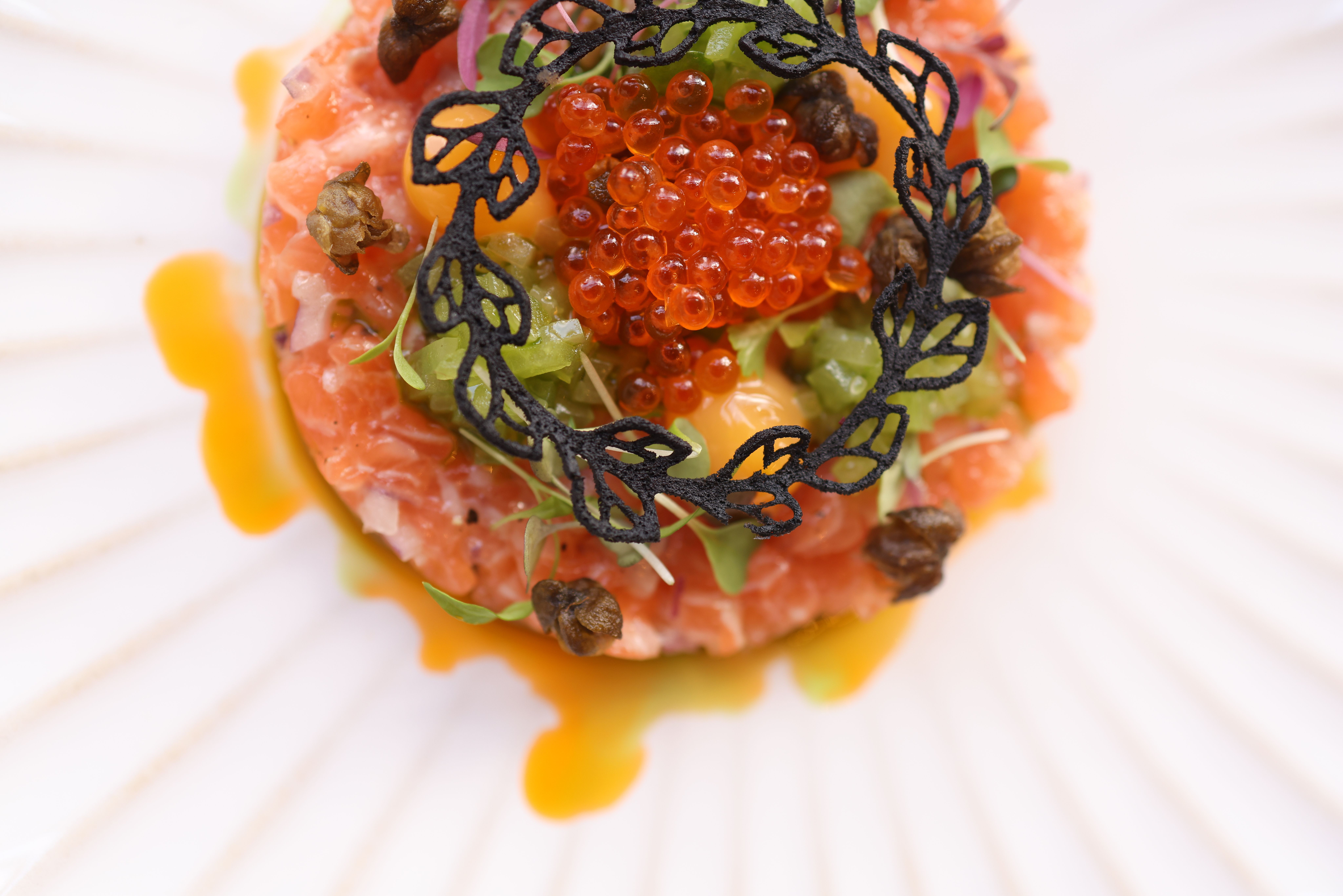 Top view of gourmet salmon tartare garnished with caviar on a decorative plate.