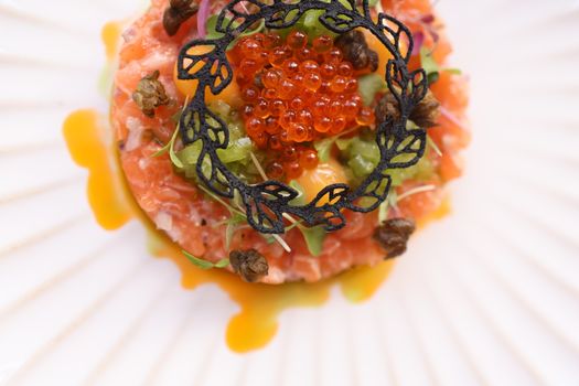 Top view of gourmet salmon tartare garnished with caviar on a decorative plate.