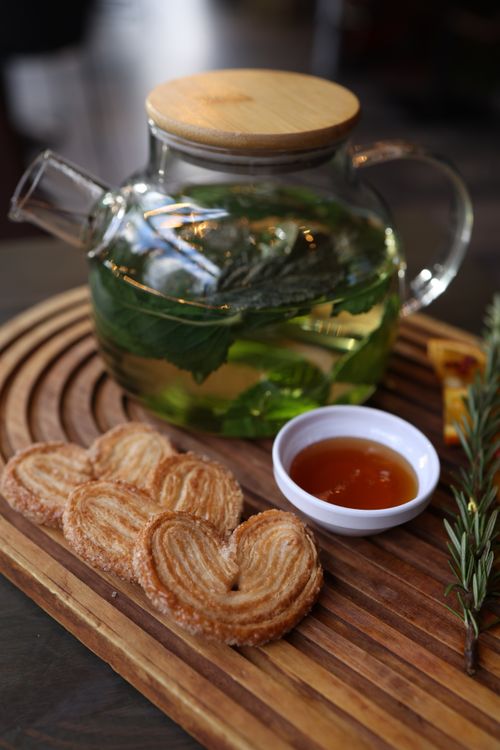 Free Glass teapot filled with mint tea alongside palmier cookies and a bowl of honey on a wooden tray. Stock Photo