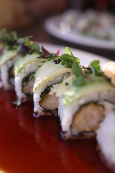Close-up of a delicious sushi roll topped with fresh avocado and microgreens.