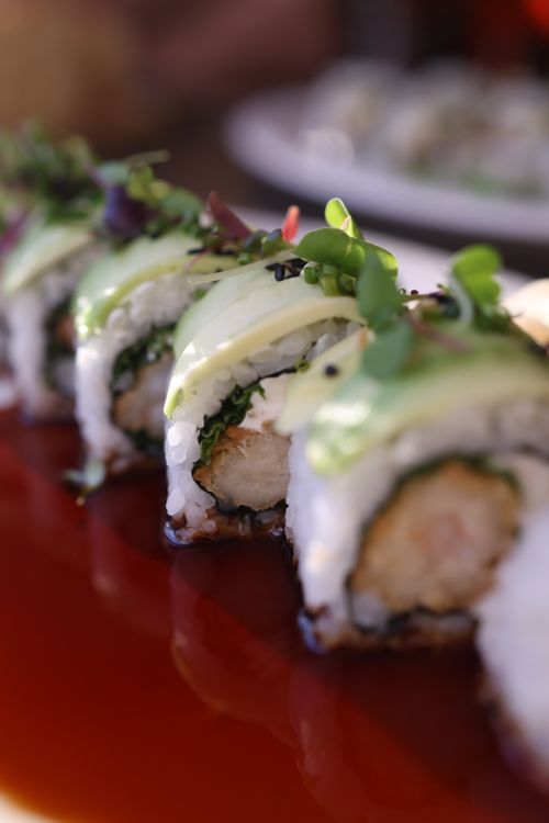 Free Close-up of gourmet sushi rolls topped with avocado and microgreens on a red plate. Stock Photo