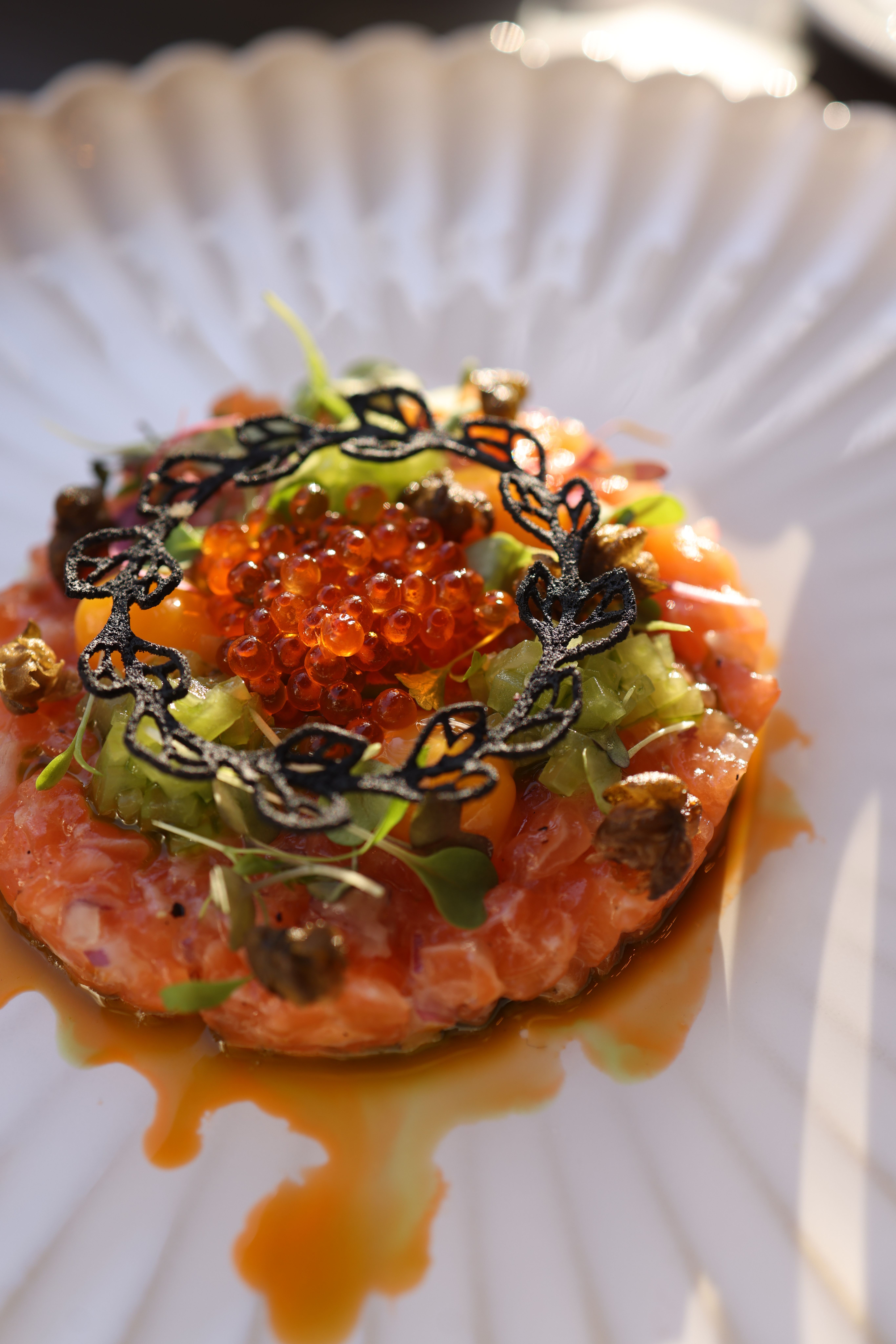 Elegant salmon tartare garnished with caviar, herbs, and a decorative sauce on a white plate.